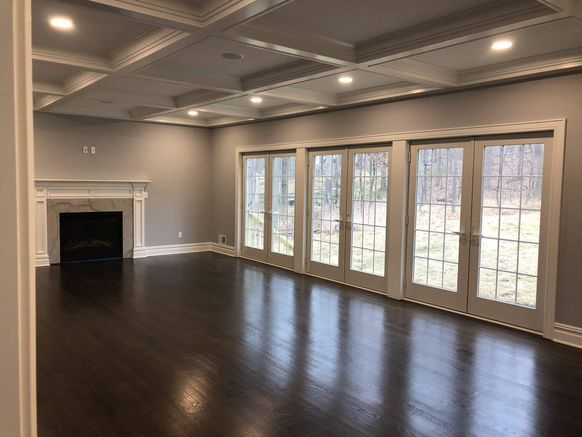 Great room with coffered ceiling, marble fireplace, and a wall of French doors